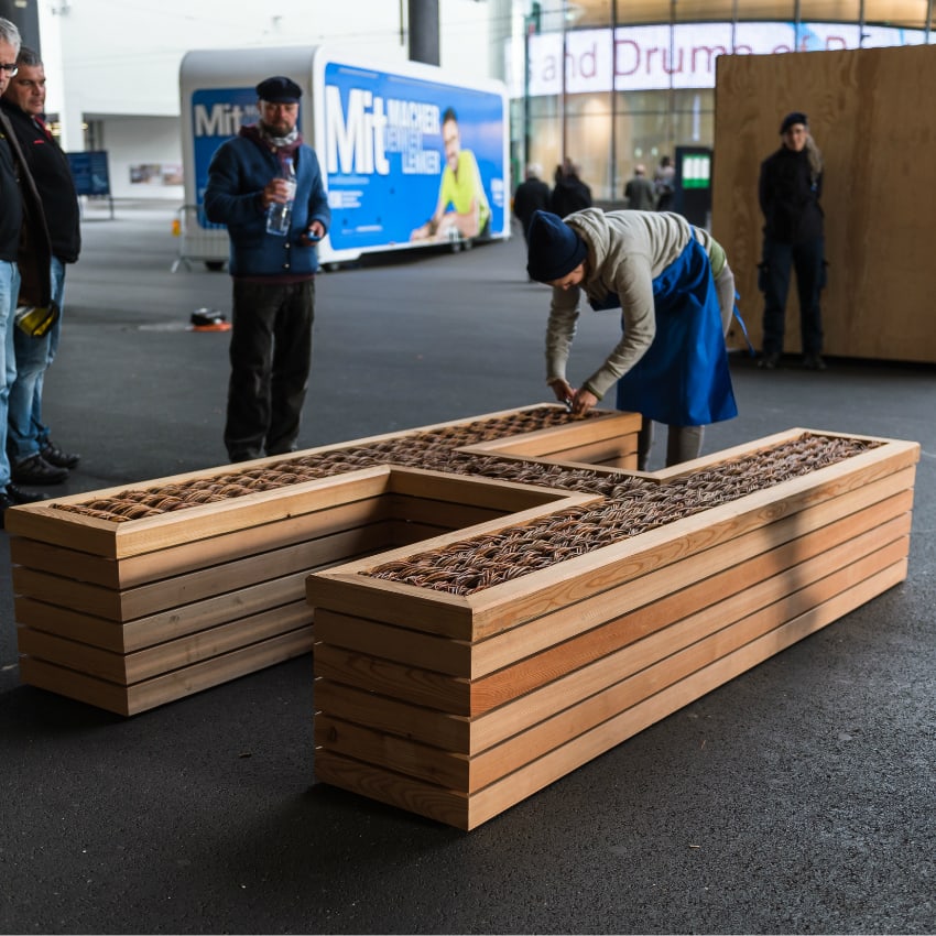 Ein Zimmermann bearbeitet ein liegendes Holz-H auf dem Messeplatz Basel.